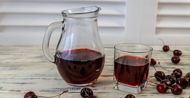 Cherry and cherry juice or wine on a wooden table a decanter and a glass with juice
