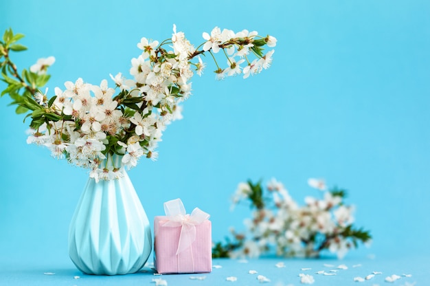 Cherry flowers in blue vase and pink gift box on blue