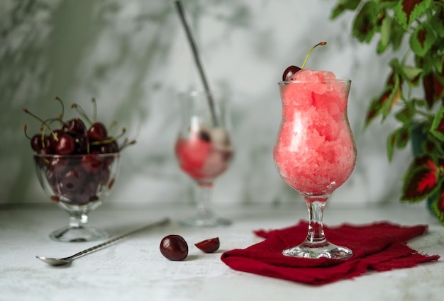 Cherry granita, berries in a glass vase and refreshing drink with ice on a light gray background