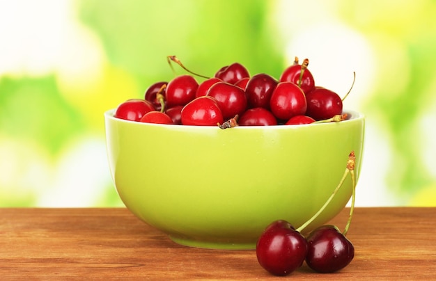 Cherry in green bowl on wooden table on green background