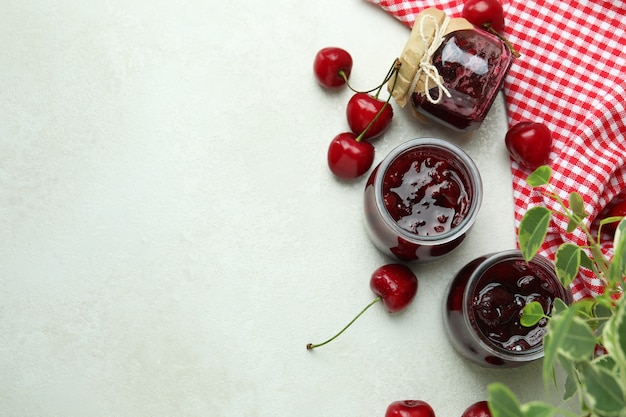 Cherry jam and ingredients on white textured table