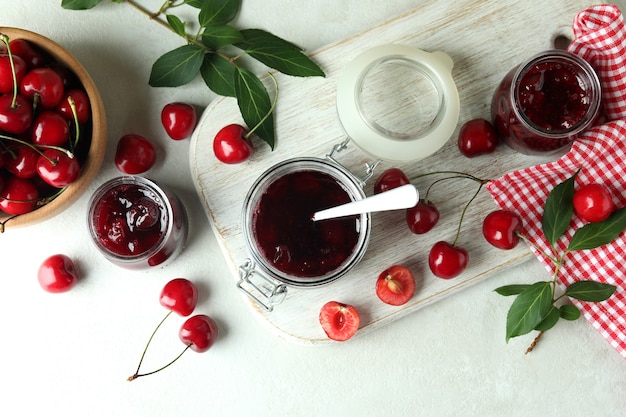 Cherry jam and ingredients on white textured table