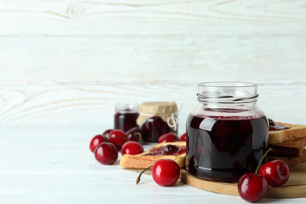 Cherry jam and ingredients on white wooden table