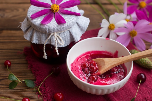 Cherry jam in a jar with a wooden spoon On a wooden background the concept of a village