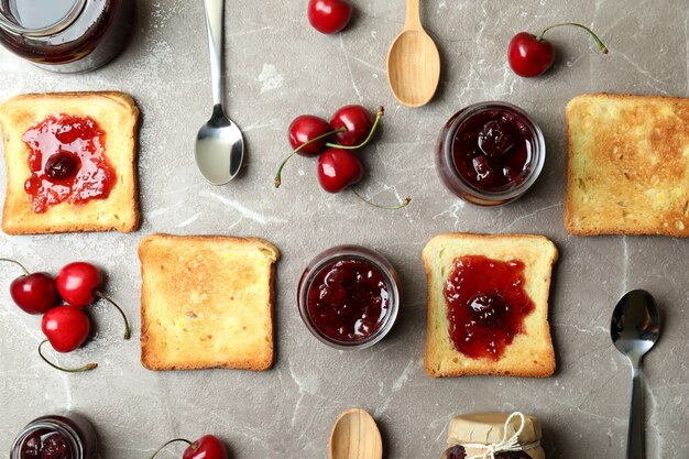 Cherry jam sandwiches and ingredients on gray textured background