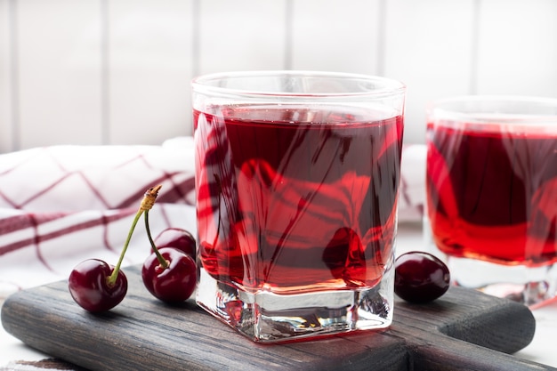 Вишневый сок в стеклянных стаканах со свежими ягодами вишни.