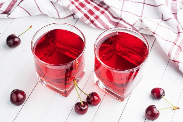 Фото Вишневый сок в стеклянных бокалах со свежими вишневыми ягодами. белый фон. ,