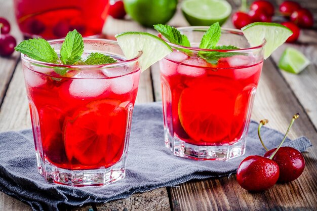 Cherry lemonade with ice lime and mint in glasses on a wooden table