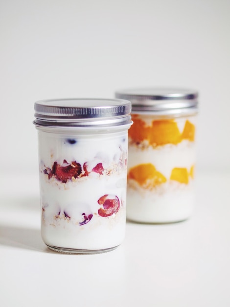 Photo cherry and mango yogurt in jars against white background