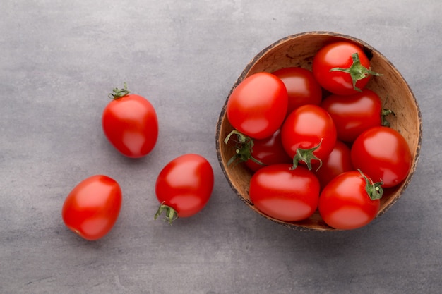 Cherry-tomaten. Drie kerstomaatjes in een houten kom op een grijze achtergrond.