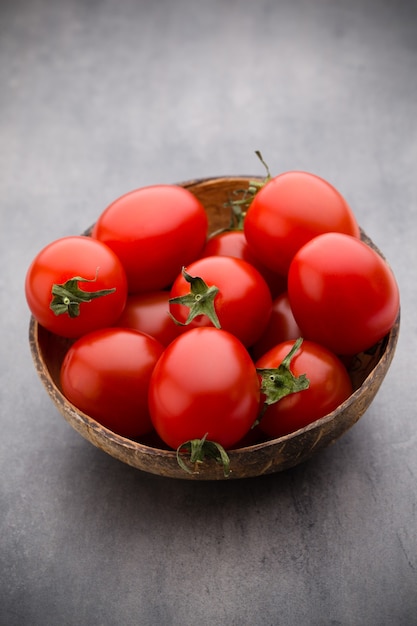 Cherry-tomaten. Drie kerstomaatjes in een houten kom op een grijze tafel.