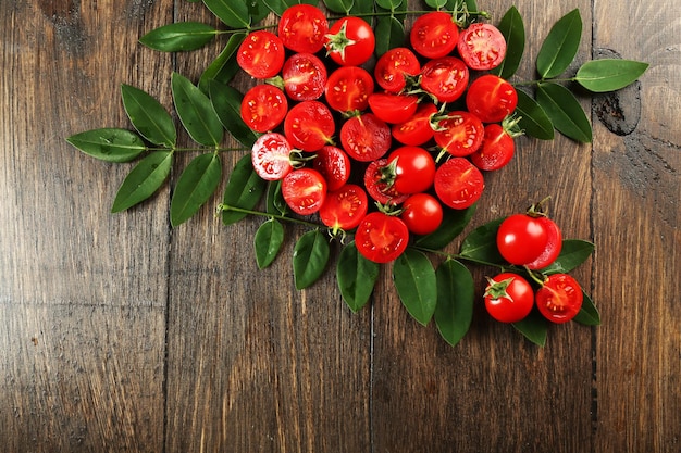 Cherry tomatoes arranged in heart shape with green leaves on wooden background