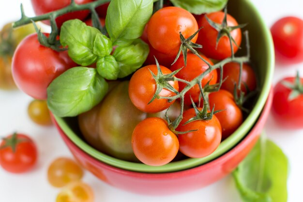 Cherry tomatoes and basil in bowl isolated on white close up