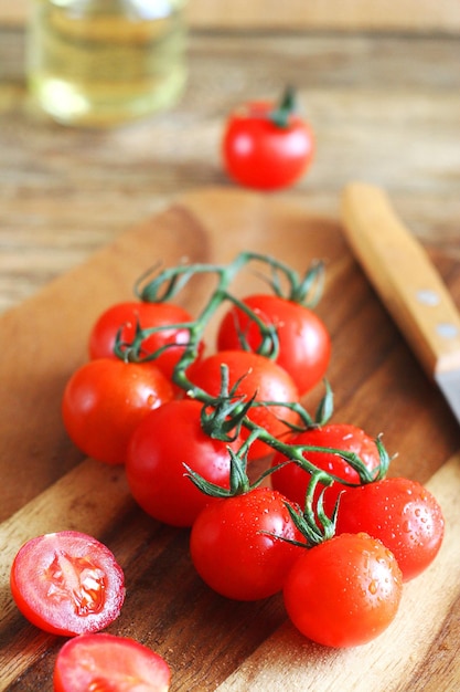 Cherry tomatoes on a branch lie on a wooden board behind there is oil and a knife lies
