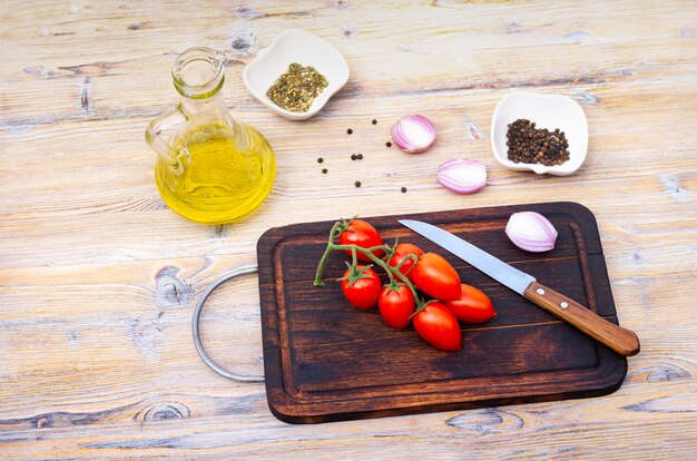 Cherry tomatoes on a branch, vegetable oil and spices on a wooden background, top view.