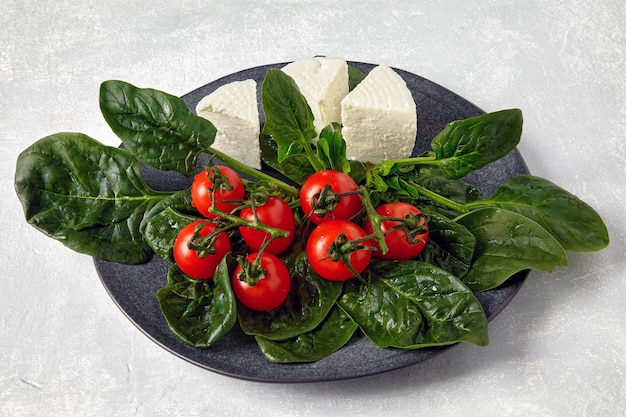 Cherry tomatoes on a branch with spinach and mozzarella cheese on a ceramic gray plate on a light stone table