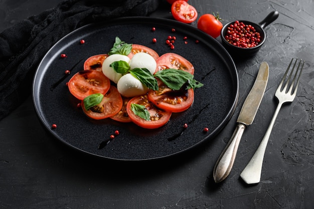 Cherry tomatoes, mozzarella buffalo cheese, basil, pesto sauce,  and spices on black slate stone chalkboard. Italian traditional caprese salad ingredients. Mediterranean food.