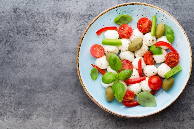 Cherry tomatoes, mozzarella cheese, basil and spices on gray slate stone chalkboard. Italian traditional caprese salad ingredients. Mediterranean food.