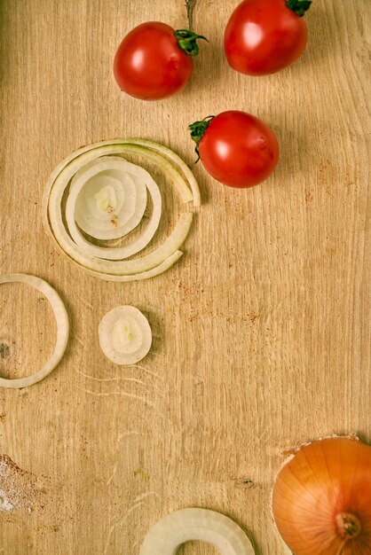 Cherry tomatoes and onion slices with green herbs on a wooden kitchen counter.