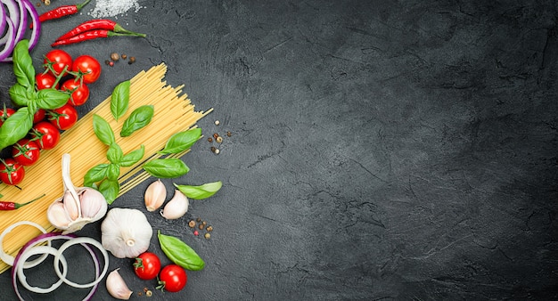 Cherry tomatoes, pasta, basil, garlic, onion, chili and peppercorns on a black concrete table, ingredients for making pasta