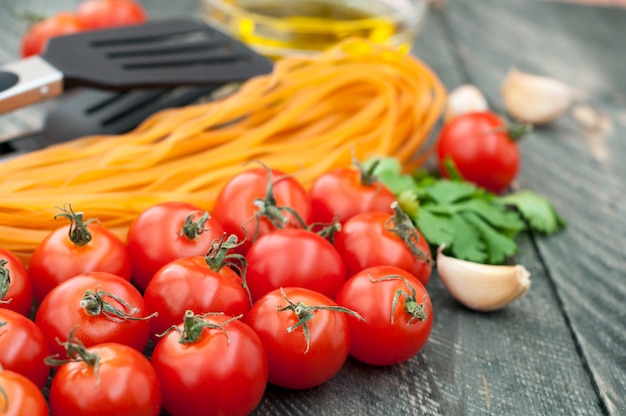 Foto tenaglie di pomodori ciliegia, pasta, olio d'oliva, aglio, erbe e pasta sullo sfondo in legno vecchio.