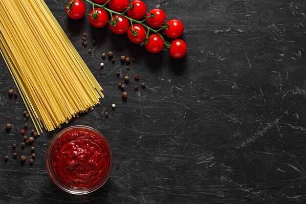 Cherry tomatoes, raw spaghetti, tomato sauce, spices. Ingredients for the Italian pasta dish, top view dark background, with space to copy text.