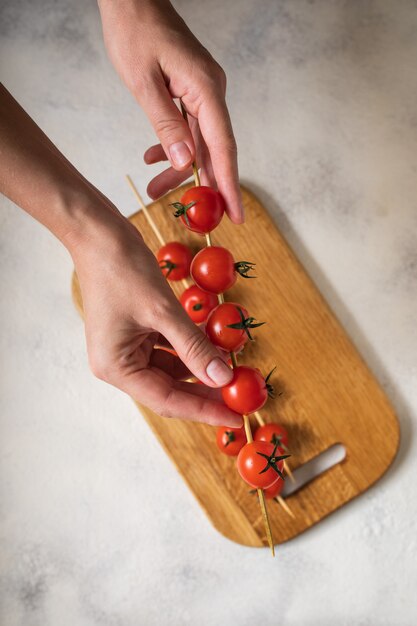 Cherry tomatoes on swords in the hands, the cooking process. View from above.