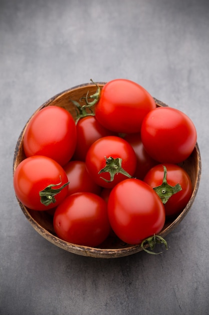 Cherry tomatoes. Three cherry tomatoes in a wooden bowl on a gray table.