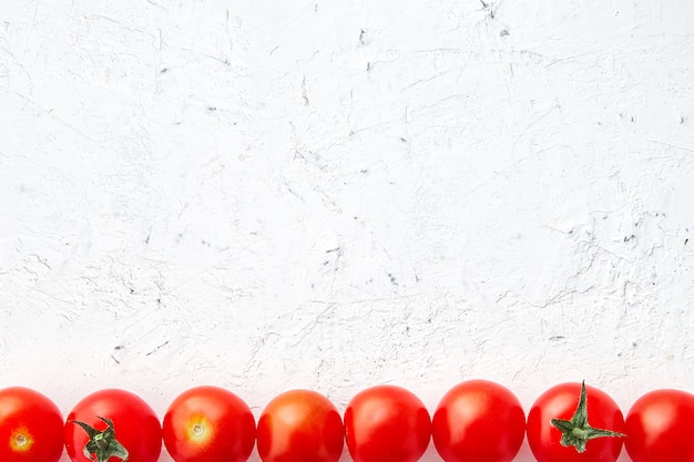 Foto pomodori ciliegia su fondo strutturato bianco.