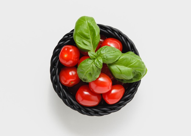 Cherry tomatoes with basil in black basket on white background