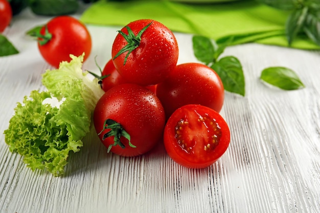 Cherry tomatoes with basil and lettuce on wooden table close up