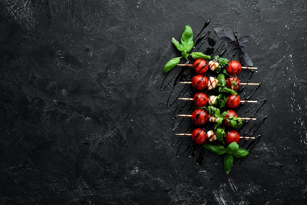 Cherrytomaatjes, mozzarella en basilicum. Op een zwarte stenen achtergrond. Italiaanse keuken. Bovenaanzicht. Vrije ruimte voor uw tekst.