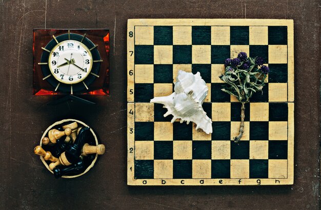 Chess, clock and seashell on old wooden background