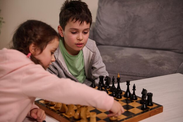 Gioco di scacchi per una mente intelligente. bellissimi bambini intelligenti: fratello e sorella si divertono, si divertono a giocare a scacchi insieme a casa. il concetto di giochi da tavolo intellettuali e sviluppo logico per i bambini