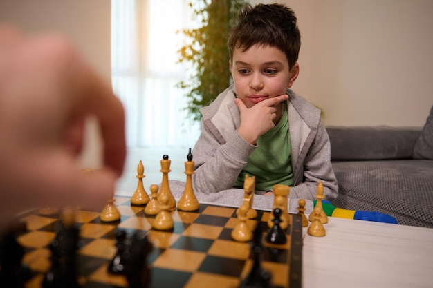 Chess game for clever mind. Handsome clever pensive teenage boy looking thoughtfully at chess board, thinking about chess strategy while playing