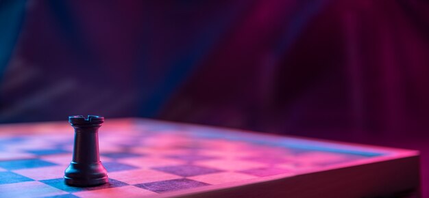 Chess pieces on a chessboard on a dark background shot in neon pink-blue colors. The figure of a chess .Close up.