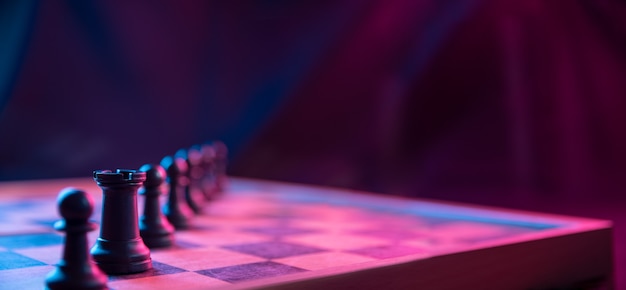 Chess pieces on a chessboard on a dark background shot in neon pink-blue colors. The figure of a chess .Close up.