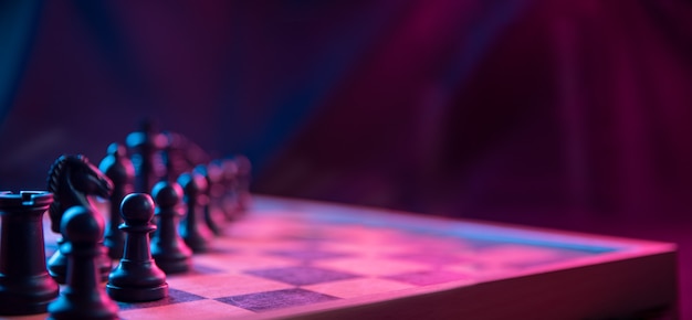 Chess pieces on a chessboard on a dark background shot in neon pink-blue colors.