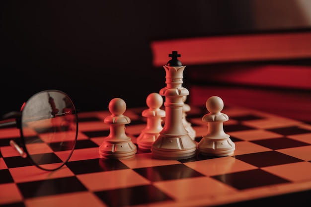 Chess pieces on the chessboard with books and glasses.