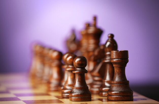 Chess pieces and game board on purple blurred background