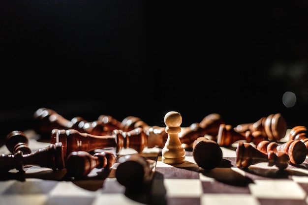 Chess strategy ideas planning and decision concept business\
winner white pawn surrounded by lying black chess pieces leadership\
strength and confidence concept good conquers evil