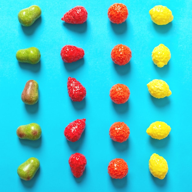 Le gomme da masticare a forma di pera, arancia, fragola e limone su sfondo blu sono disposte in file. vista dall'alto di caramelle di frutta luminose.