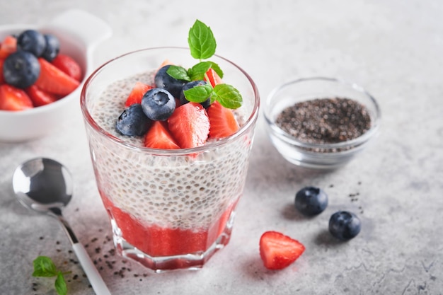 Chia aardbei pudding gezonde veganistisch ontbijt chia zaden pudding met verse bessen en munt in glas op grijze betonnen achtergrond concept van gezond eten dieet fitness menu selectieve aandacht