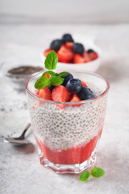 Chia aardbei pudding Gezonde veganistisch ontbijt chia zaden pudding met verse bessen en munt in glas op grijze betonnen achtergrond Concept van gezond eten dieet fitness menu Selectieve aandacht