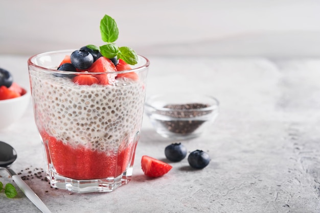 Chia aardbei pudding Gezonde veganistisch ontbijt chia zaden pudding met verse bessen en munt in glas op grijze betonnen achtergrond Concept van gezond eten dieet fitness menu Selectieve aandacht