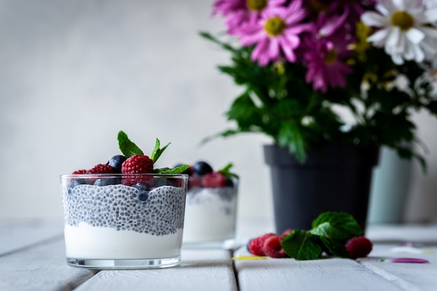 Chia met wilde bessen. Frambozen en bosbessen. Heerlijk en gezond dessert en violette bloemen over een witte houten rustieke tafel.