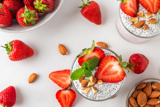 Chia pudding in glasses with fresh strawberries, almonds and mint on white surface for vegan breakfast