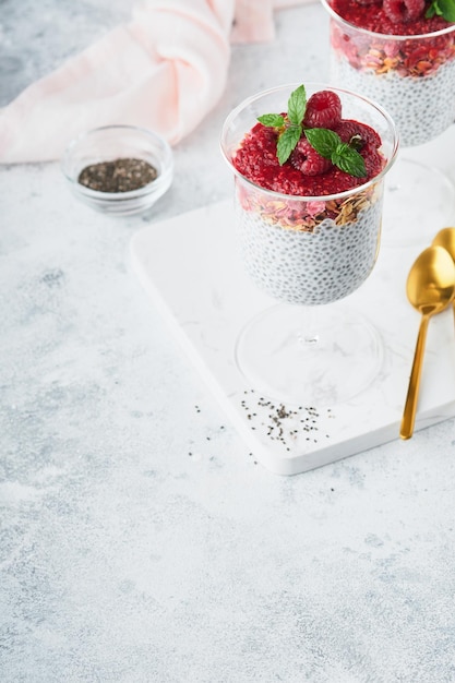 Budino di chia sano budino di chia alla vaniglia in vetro con lamponi freschi e menta su sfondo bianco colazione sana vegana