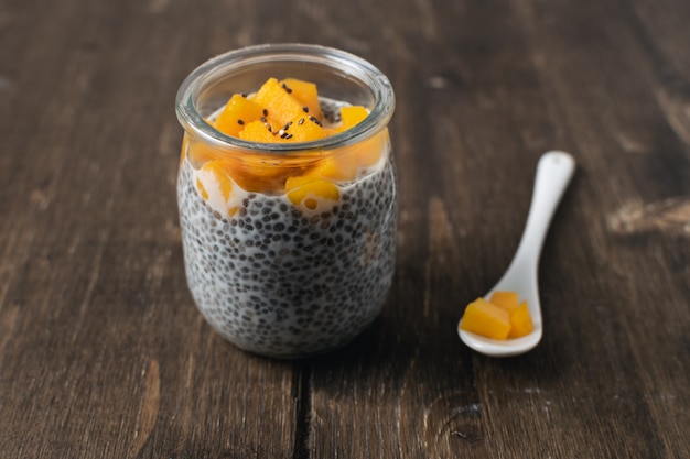 Chia-pudding in glazen pot met amandelmelk en mango op rustieke houten tafel