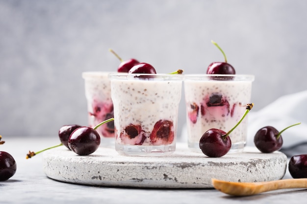 Chia pudding with cherry berries, natural yogurt, in a glass on a grey surface